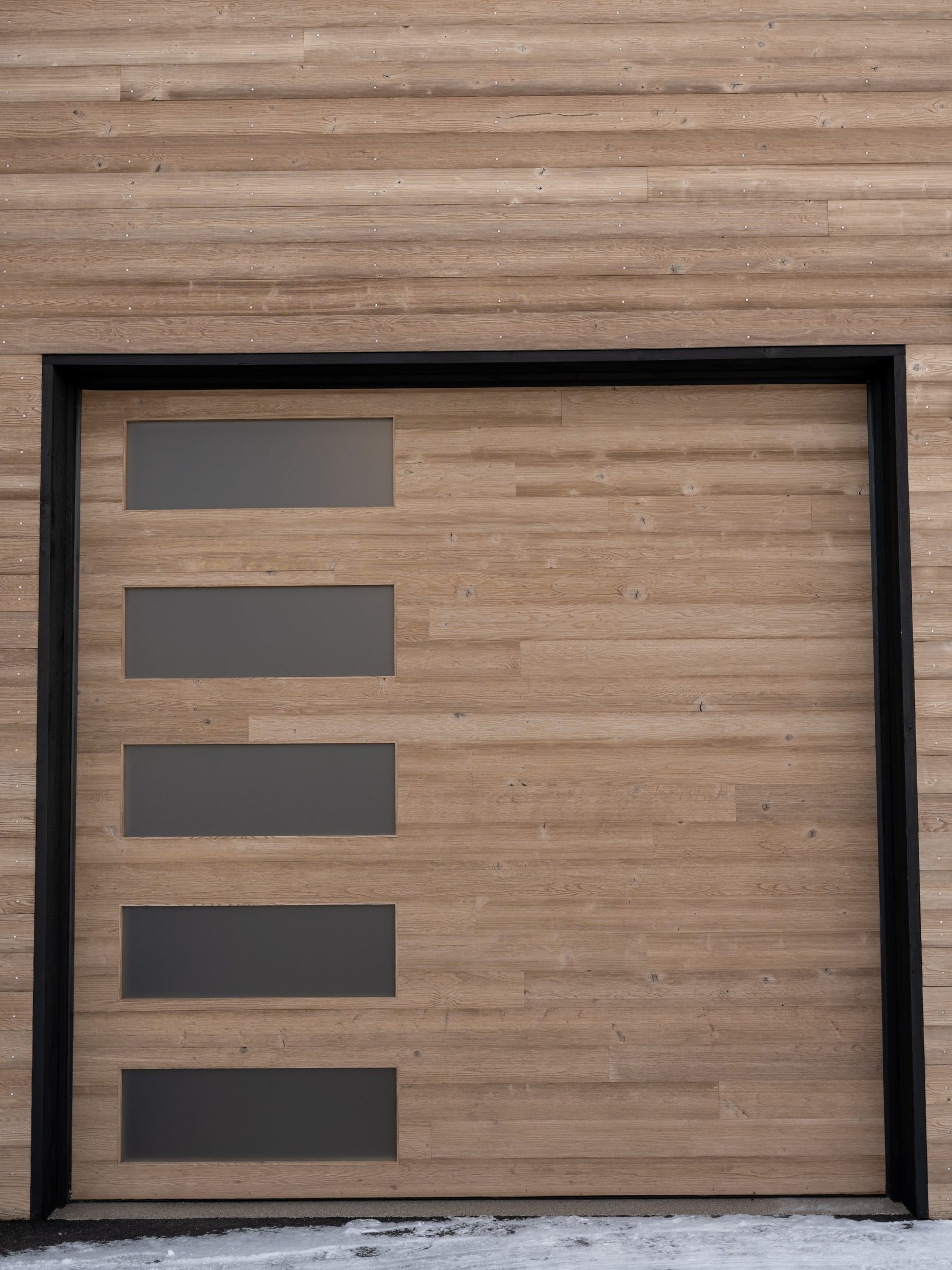 Close-up of a custom cedar garage door with four horizontal frosted glass lites and black steel frame, custom built by American Garage Door in Wheat Ridge, Colorado