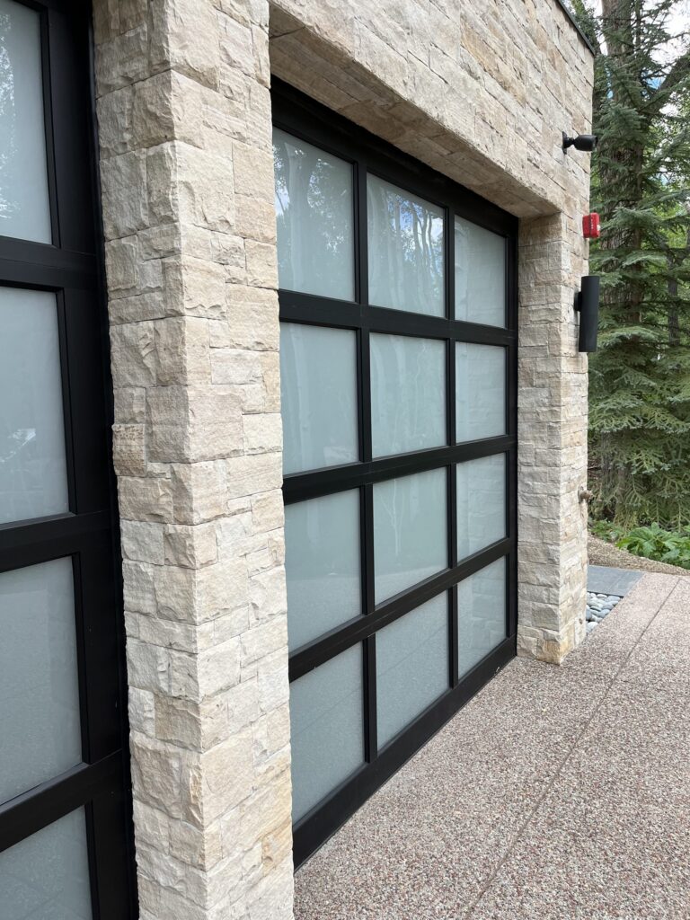 Detail of a frosted glass full-view garage door with black aluminum frame against natural stacked stone, installed by American Garage Door & Gate Systems